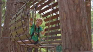 Macera parkında küçük bir çocuk. Emniyet kemeri takıyor. Yüksek bir ip patikasına tırmanıyor. Açık hava eğlence merkezi. Tırmanma faaliyetleri, kablo hatları ve her türlü engelden oluşuyor.