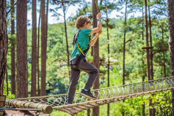 Портрет милого мальчика, идущего по веревочному мосту в парке приключений — стоковое фото