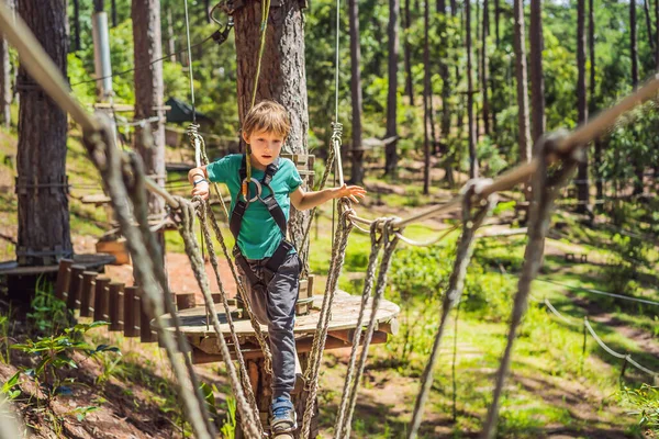 Ritratto di simpatico ragazzino che cammina su un ponte di corda in un parco di corde d'avventura — Foto Stock