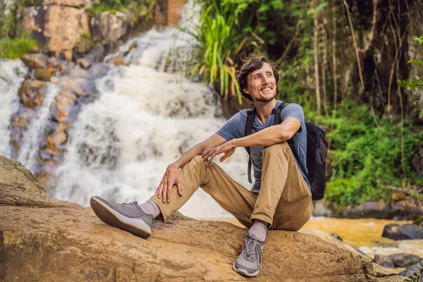 Joven con mochila de pie cerca de una cascada en el bosque. Senderista masculino en la naturaleza — Foto de Stock