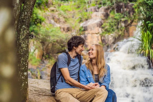 Casal de turistas com uma mochila no fundo de uma cachoeira — Fotografia de Stock