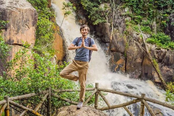 Молодой человек с рюкзаком стоит у водопада в лесу. Мужской турист в природе — стоковое фото