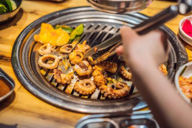 Kadın kömür ızgarasında ızgara yapıyor. Kore ya da Japon geleneksel yemek ızgarası.