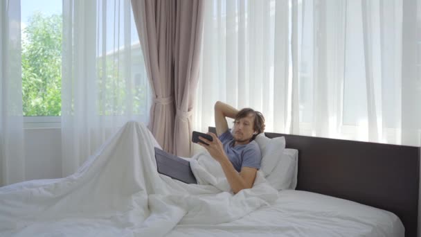 Ένας νεαρός στο κρεβάτι βλέπει κάτι σε ένα smartphone. — Αρχείο Βίντεο