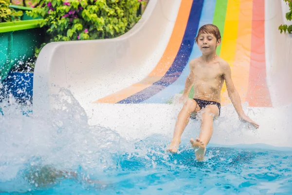 Menino ou criança se diverte salpicando na piscina depois de descer a corrediça de água durante o verão — Fotografia de Stock