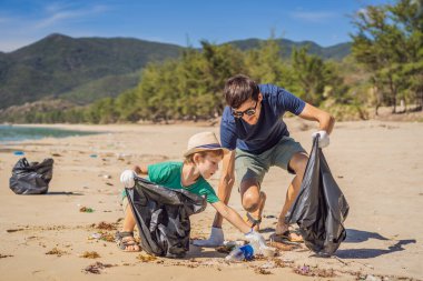 Plajı temizleyen eldivenli baba ve oğul kirli denizi temizleyen plastik torbaları topluyorlar. Çocukların doğal eğitimi. İnsan yapımı kumsalda dökülen çöplerle ilgili bir sorun.