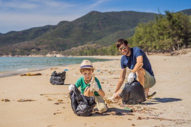 Plajı temizleyen eldivenli baba ve oğul kirli denizi temizleyen plastik torbaları topluyorlar. Çocukların doğal eğitimi. İnsan yapımı kumsalda dökülen çöplerle ilgili bir sorun.