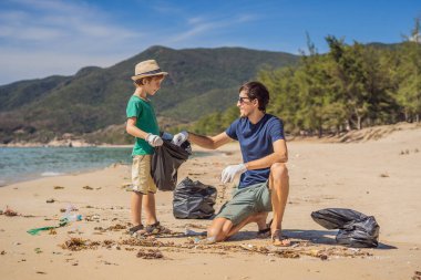 Plajı temizleyen eldivenli baba ve oğul kirli denizi temizleyen plastik torbaları topluyorlar. Çocukların doğal eğitimi. İnsan yapımı kumsalda dökülen çöplerle ilgili bir sorun.