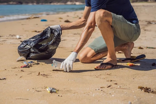 L'homme en gants ramasse des sacs en plastique qui polluent la mer. Problème des déchets déversés ordures sur la plage sable causé par la pollution d'origine humaine et de l'environnement, campagne pour nettoyer le bénévolat dans le concept — Photo