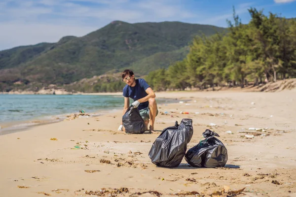 Mannen i handskar plockar upp plastpåsar som förorenar havet. Problem med spillt skräp skräp på stranden sand orsakad av föroreningar och miljö, kampanj för att rena volontären i konceptet — Stockfoto