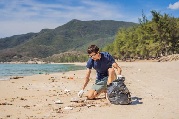 Un uomo in guanti raccoglie sacchetti di plastica che inquinano il mare. Problema dello spreco di spazzatura sulla sabbia della spiaggia causato dall'inquinamento causato dall'uomo e dall'ambiente, campagna per ripulire il volontariato nel concetto — Foto Stock