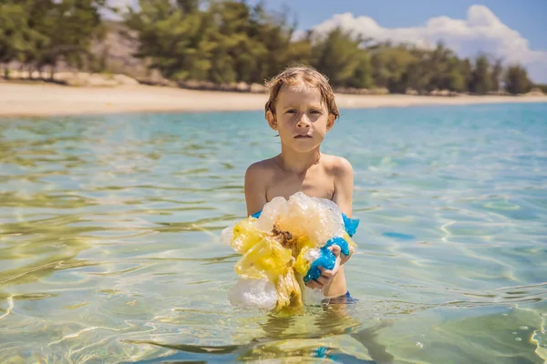 Boy collects packages from the beautiful turquoise sea. Paradise beach pollution. Problem of spilled rubbish trash garbage on the beach sand caused by man-made pollution and environmental, campaign to