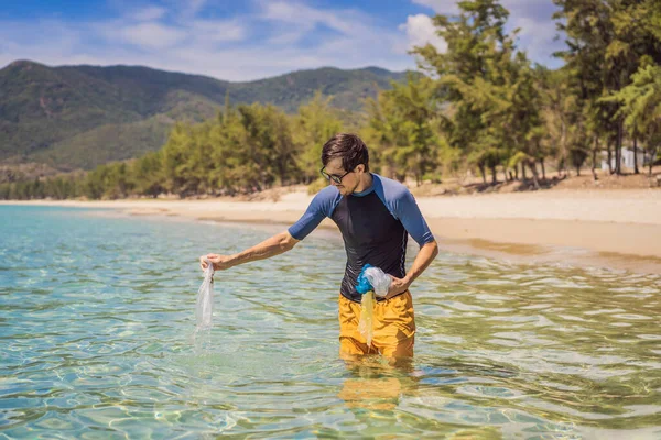 Мужчина собирает пакеты из красивого бирюзового моря. Райское загрязнение пляжа. Проблема высыпания мусора мусора на пляжный песок, вызванного техногенным загрязнением и окружающей средой, кампания по — стоковое фото