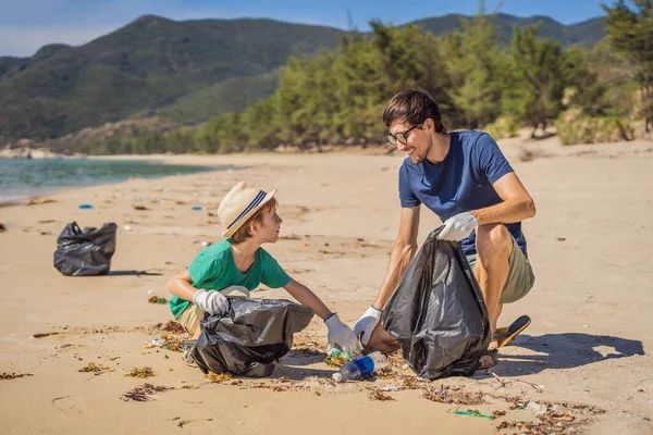 Plajı temizleyen eldivenli baba ve oğul kirli denizi temizleyen plastik torbaları topluyorlar. Çocukların doğal eğitimi. İnsan yapımı kumsalda dökülen çöplerle ilgili bir sorun.