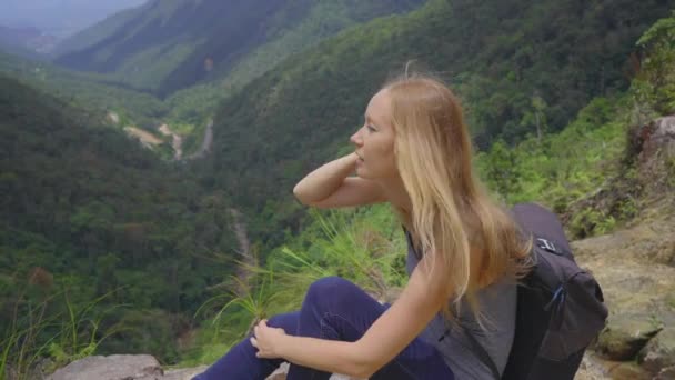 Joven viajera con una mochila en las montañas. Ella está mirando el majestuoso valle de ahí abajo. Concepto de viaje — Vídeos de Stock