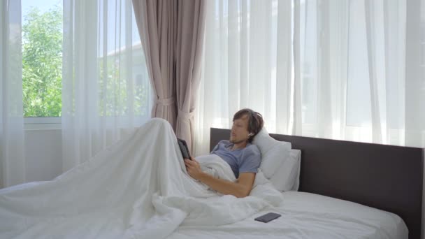 Giovane uomo disegno qualcosa con uno stilus sulla tavoletta sdraiato a letto — Video Stock