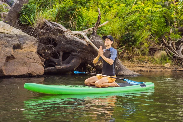 Man die yoga beoefent op een SUP board tijdens zonsopgang op een grote rivier. Stand up paddle boarding - geweldige actieve recreatie in de natuur — Stockfoto