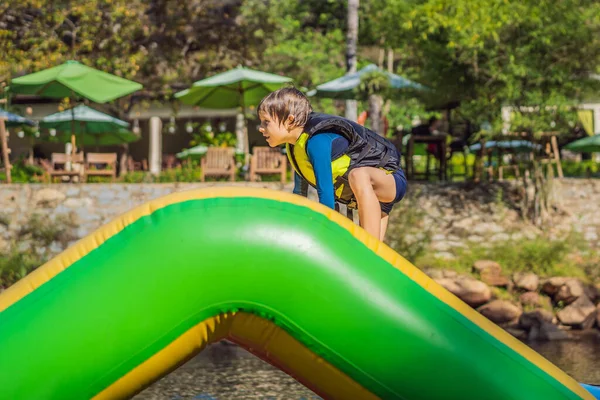 Lindo chico corre una carrera de obstáculos inflable en la piscina —  Fotos de Stock