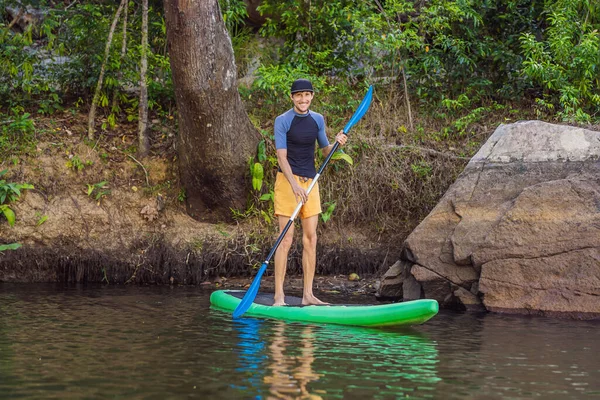 Hombre alegre está entrenando tabla SUP en el río en una mañana soleada. Stand up paddle boarding - impresionante recreación activa al aire libre —  Fotos de Stock