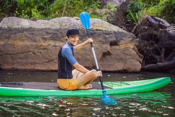 Ein fröhlicher Mann trainiert an einem sonnigen Morgen im Fluss SUP-Board. Stand Up Paddle Boarding - großartige aktive Outdoor-Erholung — Stockfoto