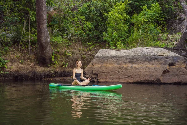 Mulher esportiva na posição de ioga no paddleboard, fazendo ioga no quadro de refeições, exercício para flexibilidade e alongamento dos músculos — Fotografia de Stock