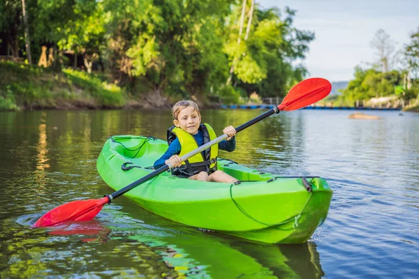 Щасливий молодий хлопчик тримає весло в каяку на річці, насолоджуючись прекрасним літнім днем — стокове фото