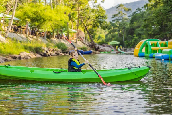 Niño feliz sosteniendo remo en un kayak en el río, disfrutando de un hermoso día de verano — Foto de Stock