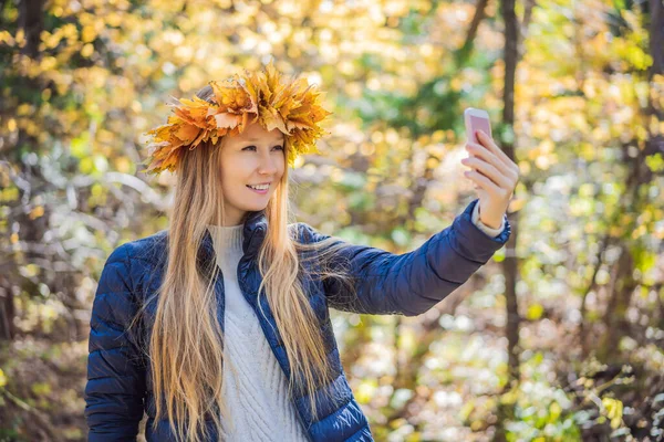 秋の葉のリースを身に着けている魅力的なブロンドの若い女性の屋外ライフスタイルのクローズアップ肖像画。笑顔で、秋の公園を歩く。スタイリッシュなニットプルオーバーを身に着けている。カエデの葉のリース — ストック写真
