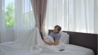 Yatakta genç bir adam tabletten bir şey izliyor ve sonra uykuya dalıyor.