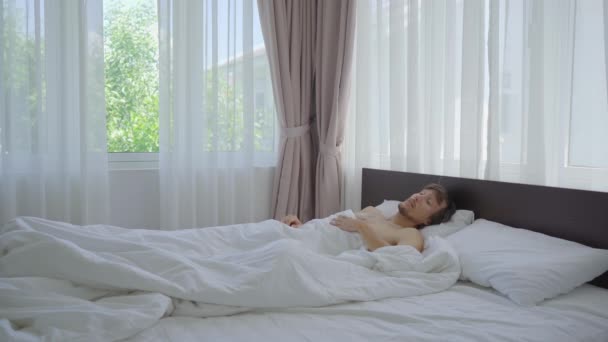 En ung man i en säng känner att det är mycket varmt — Stockvideo