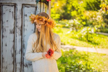 Açık hava yaşam tarzı, sonbahar yapraklarından bir çelenk takan çekici sarışın genç bir kadının yakın portresi. Şık örülü kazak giyiyor. Akçaağaç yaprağı çelengi