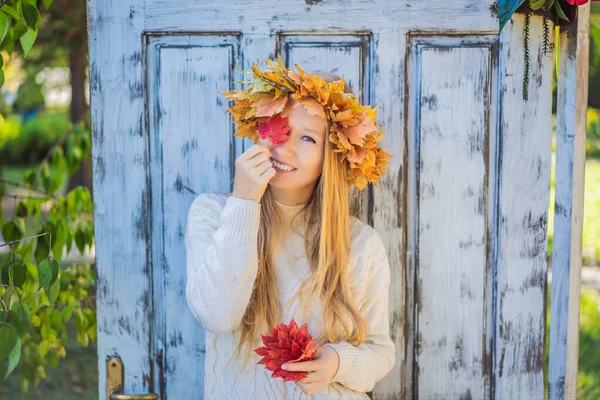 秋の葉のリースを身に着けている魅力的なブロンドの若い女性の屋外ライフスタイルのクローズアップ肖像画。スタイリッシュなニットプルオーバーを身に着けている。カエデの葉のリース — ストック写真