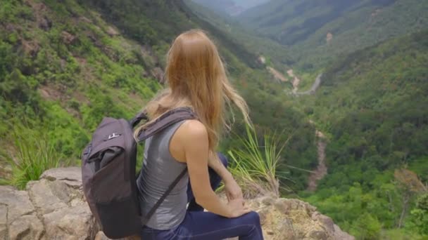 Jonge vrouw-reiziger met rugzak in de bergen. Ze kijkt naar de majestueuze vallei daar beneden. Reisconcept — Stockvideo