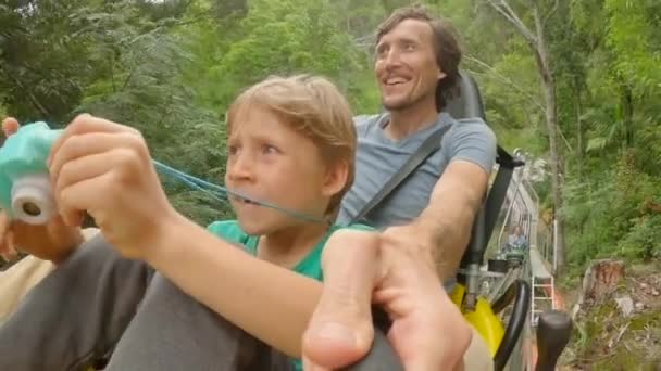 Un joven y su pequeño hijo cabalgan en una montaña rusa alpina. Disparan selfie — Vídeos de Stock