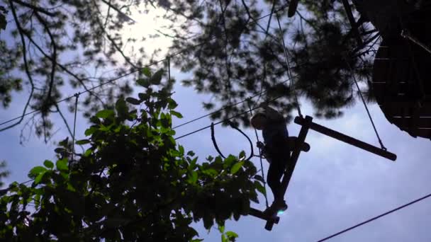 En ung kvinna i en äventyrspark. Hon har säkerhetssele. Hon klättrar på ett rep. Utomhus nöjescentrum med klättring aktiviteter bestående av zip linjer och alla typer av hinder — Stockvideo