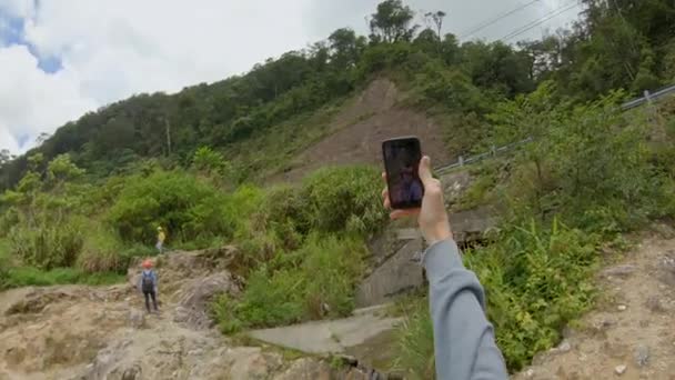 Gezichtsopname. Man in de bergen maakt foto 's en selfies met een prachtig uitzicht op een vallei daar beneden. Reis langs de weg — Stockvideo