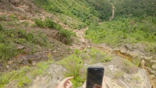 Toma de punto de vista. El hombre en las montañas toma fotos y hace selfies con una hermosa vista sobre un valle allá abajo. Concepto de viaje por carretera — Vídeos de Stock