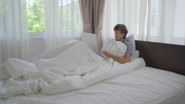 Um jovem triste em uma cama conversa com alguém através de videoconferência usando um caderno. Ele está cansado de ficar em casa durante o isolamento social — Vídeo de Stock