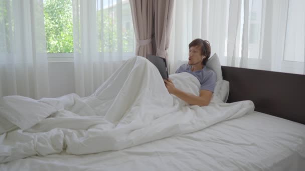 Egy fiatal férfi az ágyban vitatkozik valakivel videokonferencián keresztül. Belefáradt, hogy otthon üljön a társadalmi elszigeteltség alatt. — Stock videók