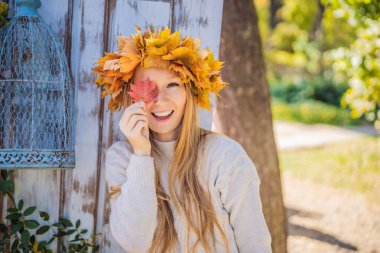 Açık hava yaşam tarzı, sonbahar yapraklarından bir çelenk takan çekici sarışın genç bir kadının yakın portresi. Şık örülü kazak giyiyor. Akçaağaç yaprağı çelengi