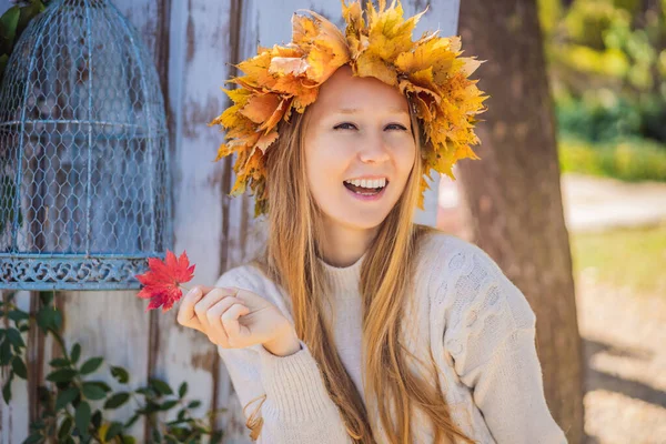 Outdoors lifestyle close up portrait of charming blonde young woman wearing a wreath of autumn leaves. Wearing stylish knitted pullover. Wreath of maple leaves — Stock Photo, Image