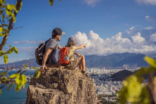 Father and son local tourist sits on a rock and enjoys the view of her city. Local tourism concept. Tourism after COVID 19 — Stock Photo, Image