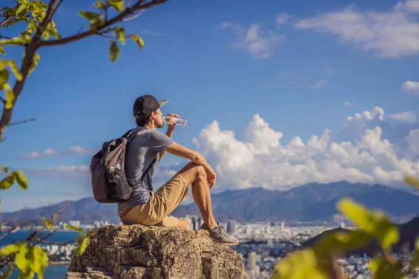 Een jonge man lokale toerist zit op een rots en geniet van het uitzicht op haar stad. Lokaal toeristisch concept. Toerisme na COVID 19 — Stockfoto