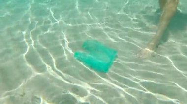 Güzel turkuaz denizde plastik poşet toplayan bir adamın sualtı çekimi. Cennet kumsalı kirliliği. İnsan yapımı kirliliğin neden olduğu kumsaldaki çöp sorunu. Eko kampanyaları