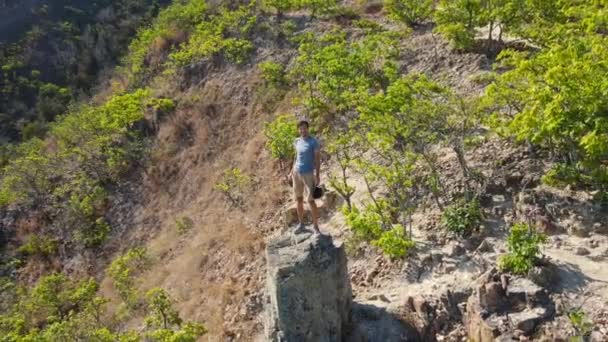 Un disparo aéreo de un joven sentado en una roca en las montañas. Concepto de senderismo — Vídeo de stock