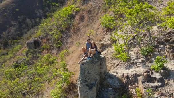 Vue aérienne d'un jeune homme et d'une jeune femme assis sur un rocher dans les montagnes. Concept de randonnée — Video