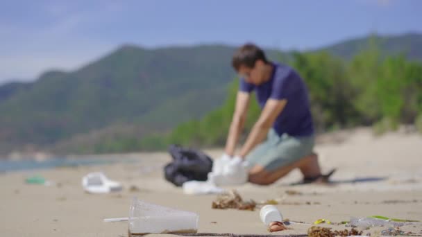 Mann mit Handschuhen sammelt Plastikmüll am Strand ein. Das Problem des Mülls am Strand Sand verursacht durch menschengemachte Verschmutzung. Öko-Kampagnen für saubere Umwelt. Ökologisches Freiwilligenkonzept — Stockvideo