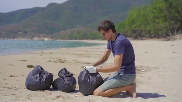 Een man met handschoenen verzamelt plastic afval op een strand. Het probleem van afval op het strand zand veroorzaakt door door door de mens veroorzaakte vervuiling. Eco-campagnes om het milieu te reinigen. Ecologisch vrijwilligerswerk — Stockvideo