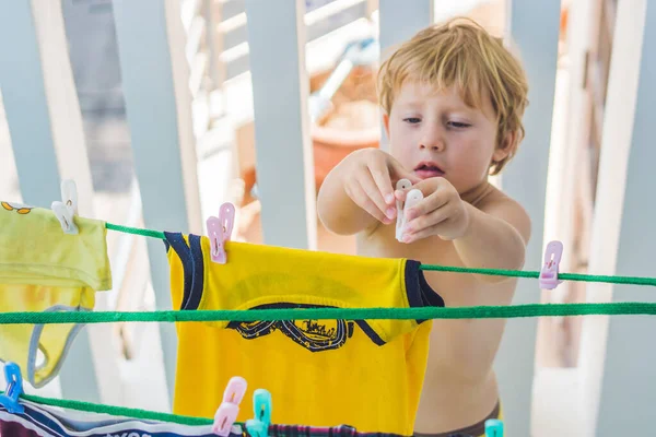 A little boy helps her mother to hang up clothes