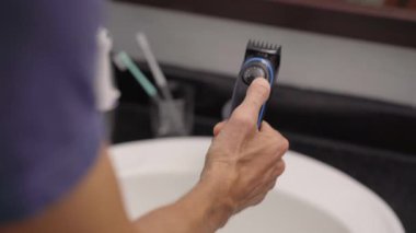 Sakalını sakal kesme makinesiyle kesen genç bir adamın yakın plan fotoğrafı.